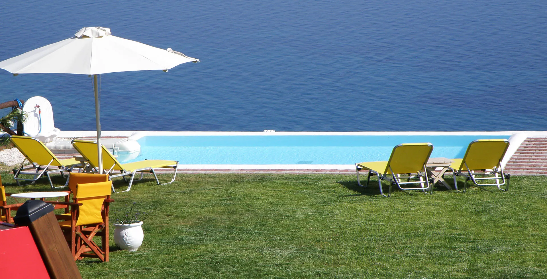 Infinity pool and sun loungers on the lawn, with the Aegean Sea beyond