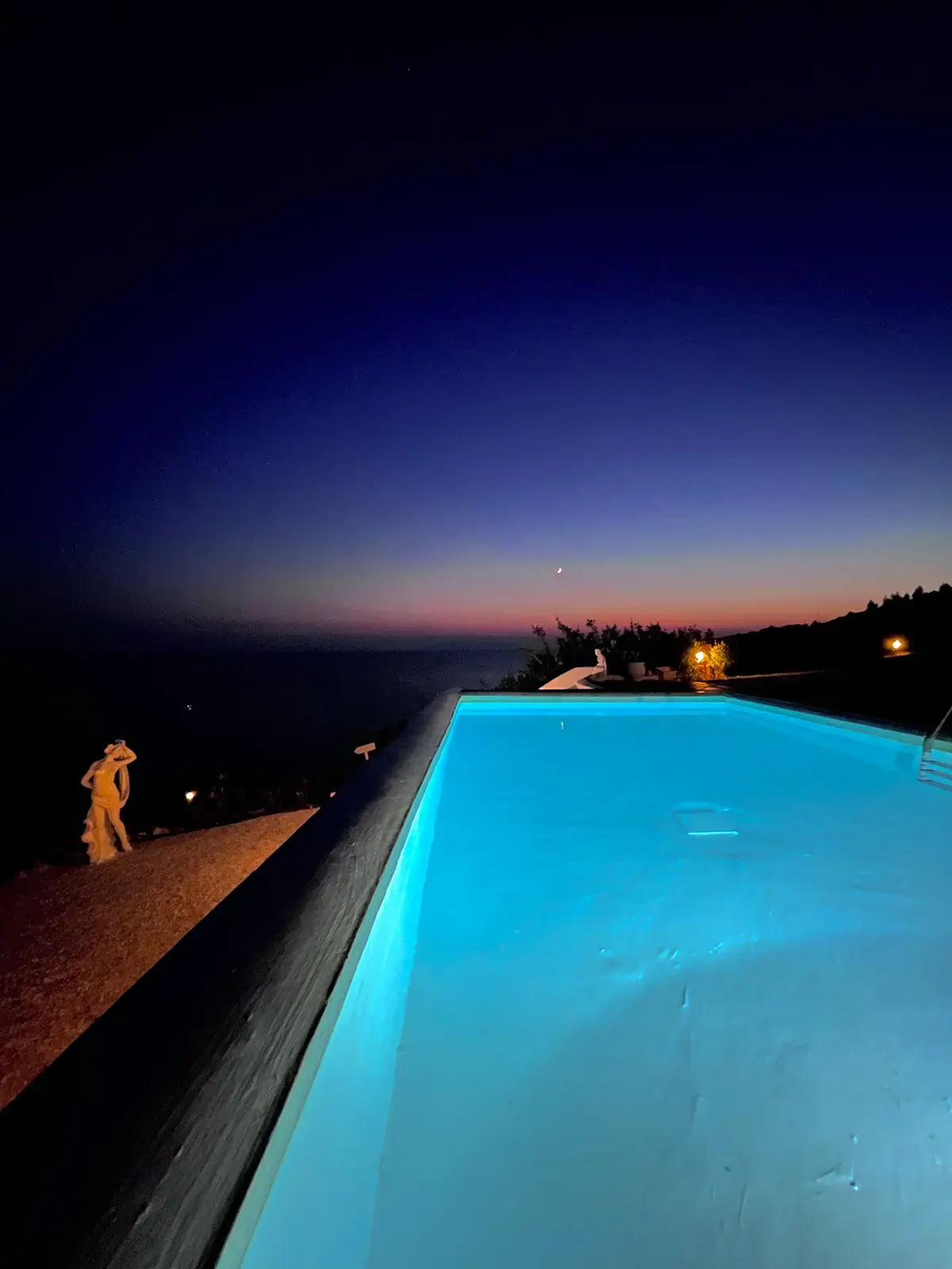 Lit infinity pool at night above the dark sea