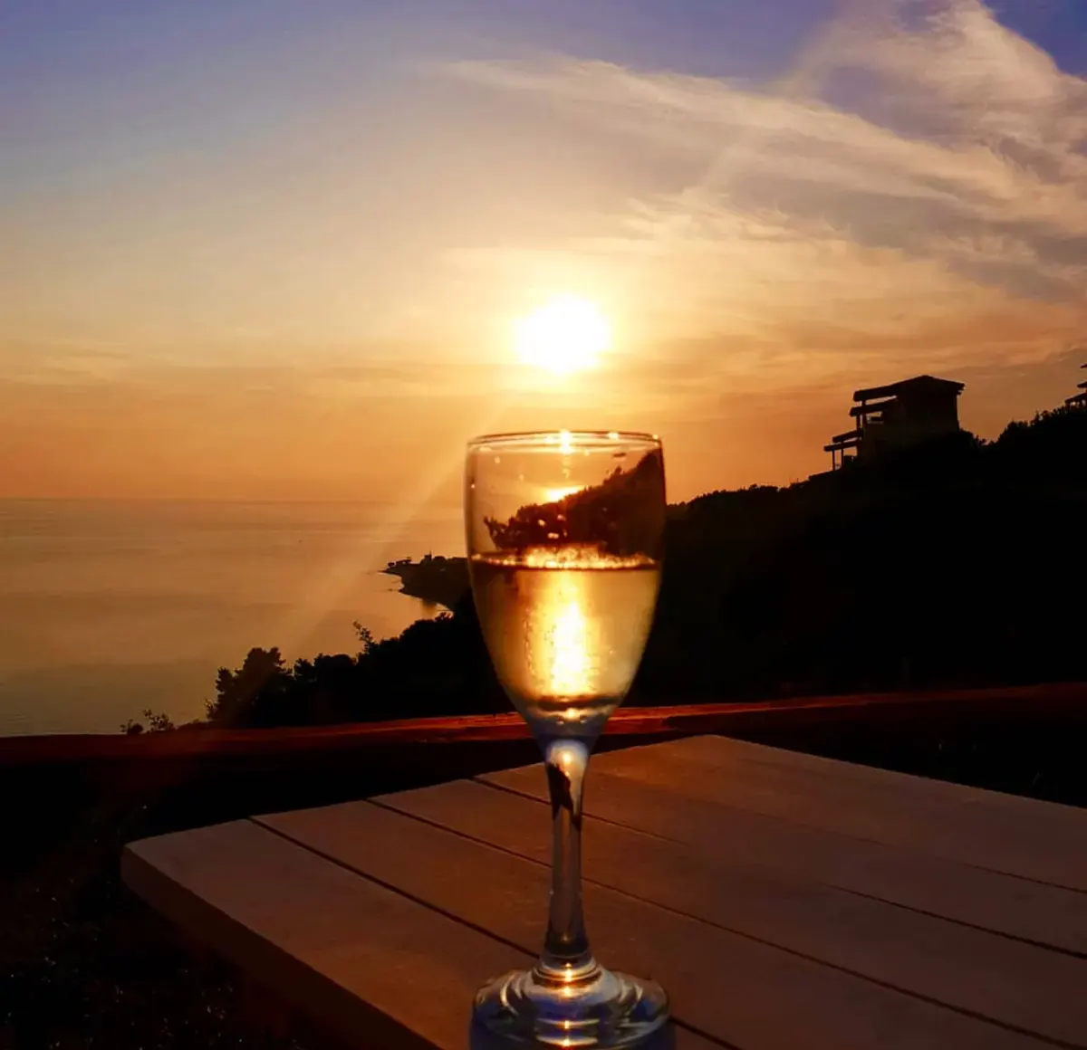 A glass of wine on a terrace table as the sun sets over the sea
