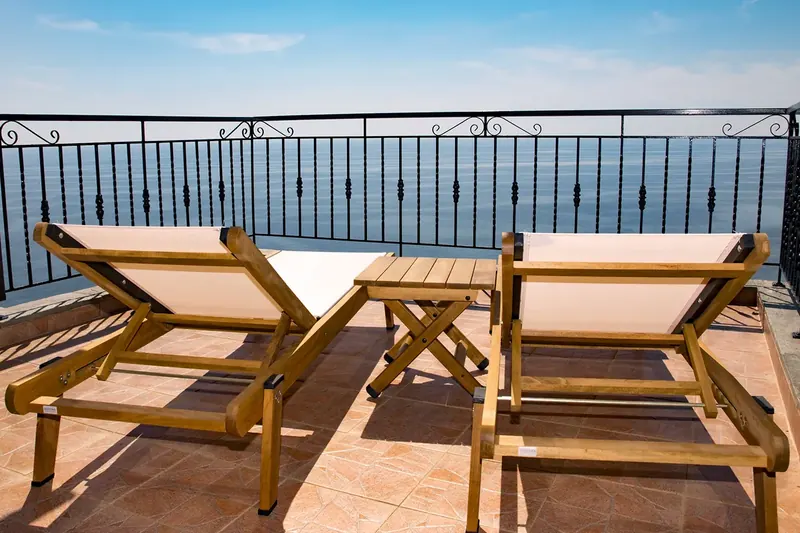 Two wooden sun loungers on a balcony above the sea